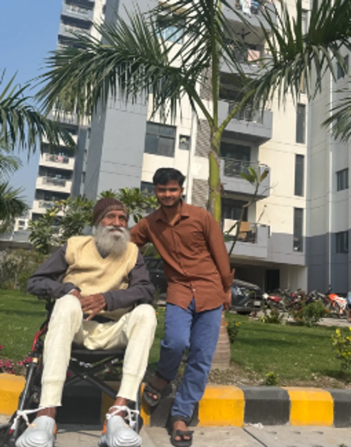 Patient attendant standing with an elderly man on a wheelchair outside a residential society in Greater Noida